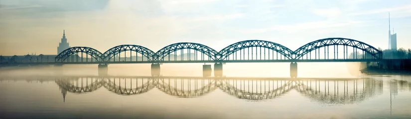 Fototapete Brücken Silhouette der Rigaer Eisenbahnbrücke im nebligen frühen Morgen