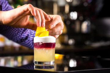 Closeup image of bartender hands decorating cocktail with lemon at dark backgrpund.