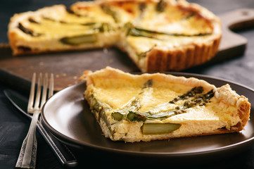 Homemade tart with asparagus and cheese on black background.
