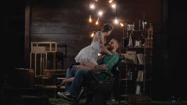 Erotic girl is going to shave her beard to a brutal man who sits on a hairdresser's armchair in a vintage location in Slow motion. Sexy girl with a dangerous razor in her hands boldly kisses a client