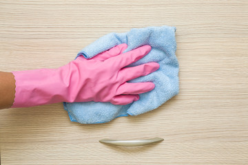 Hand in pink rubber protective glove with rag wiping a cupboard in the room. Early spring cleaning or regular clean up. Maid cleans house.