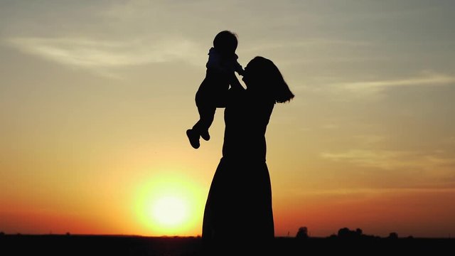 Happy child rushes into hands of mother. Family hugs over sunset sky background. Silhouettes of anonymous boy and woman outside in summer or autumn landscape. Slow motion 180fps