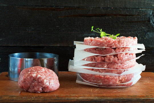 Stack of raw homemade beef burgers on a wooden cutting board with some minsed meat and metal form on a background. Home healthy eating