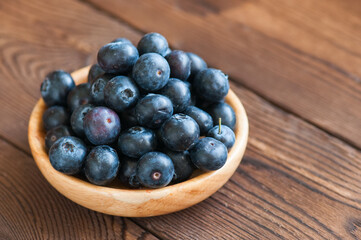Close up of fresh raw blueberries served in a wooden plate. Wooden background and copy space. Helthy eating and gardening concept.