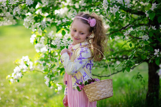 Beautiful smiling cute girl with a basket of flowers in a blooming apple-tree in a summer day