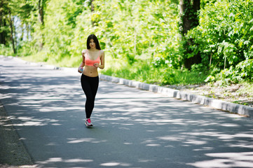 Fitness sport girl in sportswear run at road in forest with bottle water on hand, outdoor sports,...