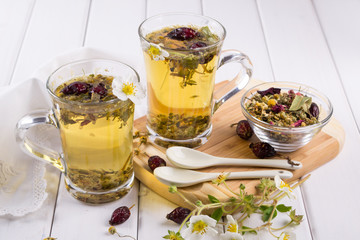 Two cups of herbal tea with rosehip , chamomile, herbs on  white wooden table