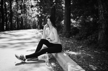 Fitness sport girl in sportswear sitting at road in park with water at bottle, outdoor sports, urban style.