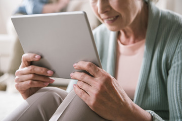 cropped shot of senior woman using digital tablet while sitting at home