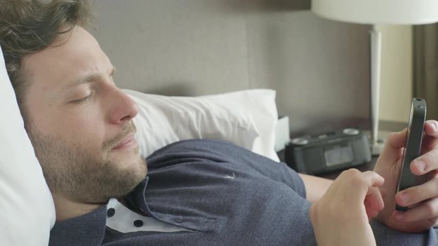 Man lying in bed looking at smart phone