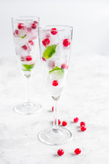 frozen red berries in ice cubes with mint in glasses on stone background