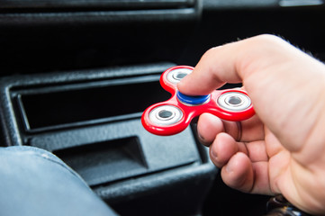 Close-up of a man's hand playing with a spinner while in a traffic jam on the background of the car's interior