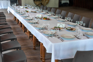 Interior of the restaurant, cafe. Tables with utensils, plates, wiches, knives, glasses and wine glasses, and brown chairs, preparation for celebration. Horizontal frame