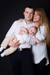 Portrait of Happy and smiling young parents mother and father - playing With Their Baby boy 4 month old on black background.