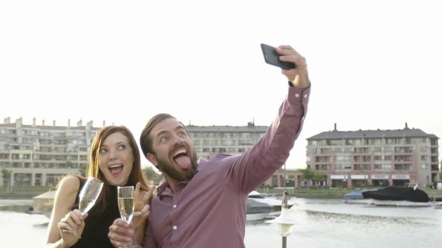 Couple posing for selfie while drinking champagne outdoors