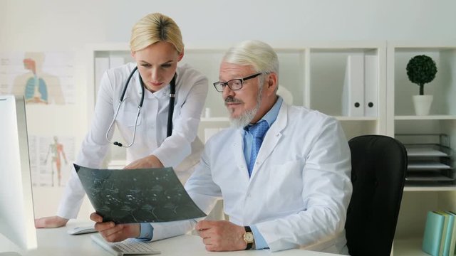 Midle aded caucasian senior doctor man and young caucasian female doctor looking x-ray image and talking about it. Indoor.