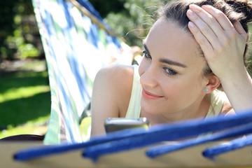 Letni relaks w ogrodzie. Młoda atrakcyjna kobieta wypoczywa na hamaku w ogrodzie rozmawiając przez telefon