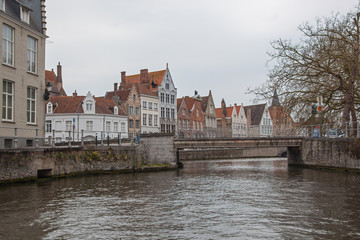 Naklejka premium Historic medieval buildings along canal in the tourist center of Bruges (Brugge) on a cloudy day, Belgium