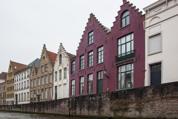 Fototapeta na wymiar View of the picturesque facades of historic buildings from canal in the tourist center of Bruges (Brugge) on a cloudy day, Belgium
