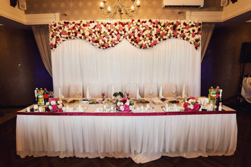 Dinner table for newlyweds decorated with red ribbons and flowers