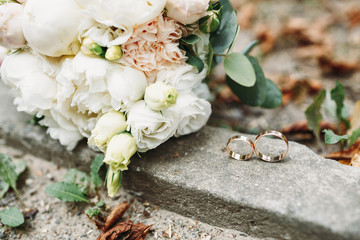 Golden wedding rings lie before white bouquet on the ground
