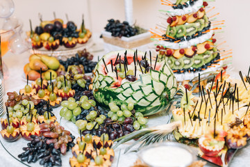 Watermelon with fruits and grape stands among onther fruits on the table