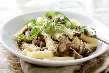 Italian traditional pasta with mushrooms and arugula in white bowl