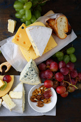 Assortment of fresh Cheeses, Grapes, Bread and Walnuts on wooden background
