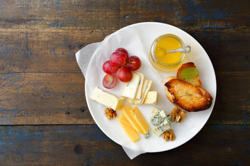 Cheese plate with honey, grapes, bread and walnuts on old wooden board