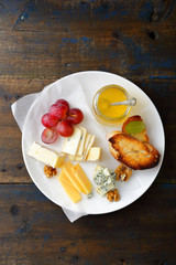 Cheese plate with honey, grapes, bread and walnuts on old wooden background