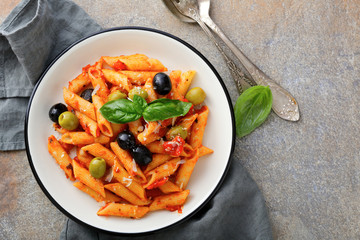 Pasta Penne in tomato sauce with basil and olive on a slate background