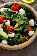 Fresh Avocado Salad with cherry tomatoes, olive, mozzarella and arugula closeup