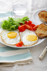 Breakfast - Fried Eggs, bread, tomato and lettuce on a plate