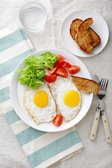 Breakfast - Fried Eggs, tomato, lettuce, bread and water glass on the striped napkin