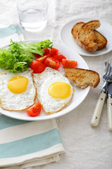 Fried Eggs with bread, tomato and lettuce on a white plate