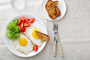 Fried Eggs with lettuce, tomato and bread on a linen tablecloth
