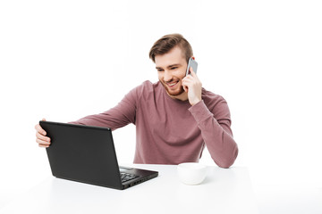 Smiling young man looking at the display of computer talking on the phone and holding laptop display isolated