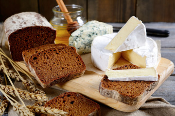 Brie cheese, black bread slices, roquefort and honey on a board