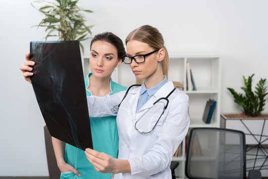Serious doctor in eyeglasses and nurse examining x-ray image in hospital