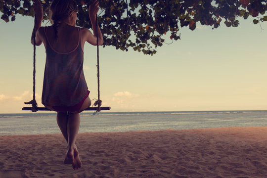 Girl swinging on a sandy beach with ocean / sea view.