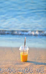 Orange juice in a disposable cup in the sand on the beach