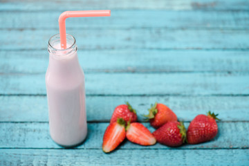 Close-up view of tasty milkshake in glass bottle with drinking straw and fresh strawberries on wooden table