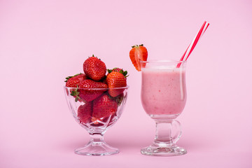 delicious strawberry milkshake in glass with straw and fresh strawberries in bowl isolated on pink