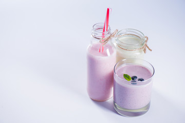 fresh berry milkshakes in glassware with straw isolated on purple