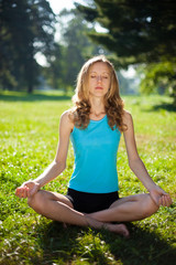 Young girl in lotus pose in the summer park