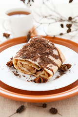 Piece of apple pie strewn grated chocolate with tea on a plate