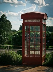 View of sunlit old red telephone booth against sky