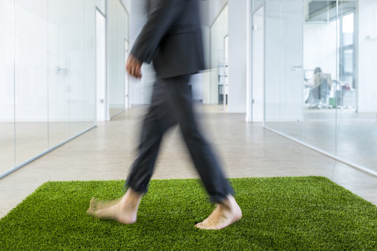 Mature businessman walking barefoot on grass carpet in office - Powered by Adobe