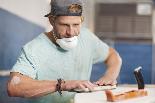 Surfboard shaper workshop, surf shop employee sanding surfboard