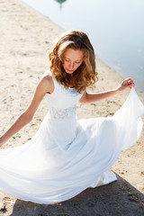 Elegant young girl bride in a white dress on a sandy river beach